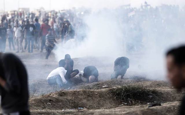 متظاهرون وسط الغاز المسيل للدموع بمحاذاة السياج في قطاع غزة، آذار/مارس 2019.