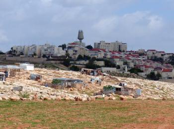 Houses in the Palestinian Bedouin community of Arab al Jahalin al Jabal, east of Jerusalem, against the backdrop of the Israeli settlement of Ma’ale Adummim. © Photo by OCHA.