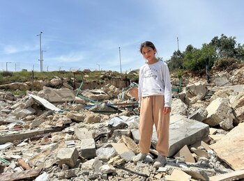 A girl in Az Za’ayyem Bedouin community (Jerusalem governorate) stands on what remains of her home following its demolition by Israeli authorities due to the lack of building permits, which are rarely granted to Palestinians, April 2026. Photo by OCHA