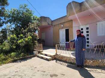 אום סאלח שרייתח עומדת בחזית ביתה באל־מזרעה אל־קיבלייה, מרכז הגדה המערבית. צילום: משרד האו״ם לתיאום עניינים הומניטריים.