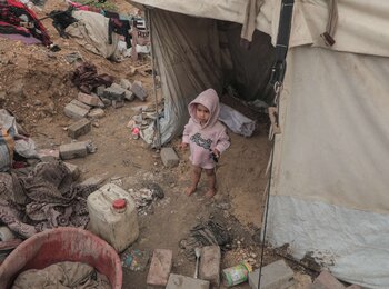 A toddler stands amid debris and personal belongings outside a tent in the Gaza Strip. Photo by UNICEF.