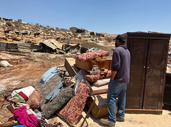 A Palestinian man next to some of his belongings, out in the open, following the demolition of 20 homes and other structures in Al Mughayyir. Photo by OCHA