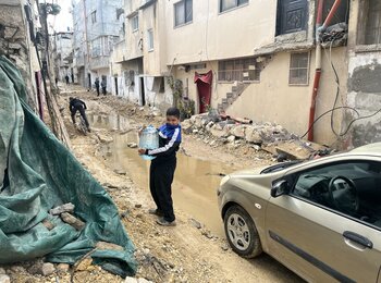 A Palestinian boy carrying water through a heavily damaged street of Tulkarm refugee camp, following an Israeli operation that involved drone strikes and road bulldozing. Photo by OCHA