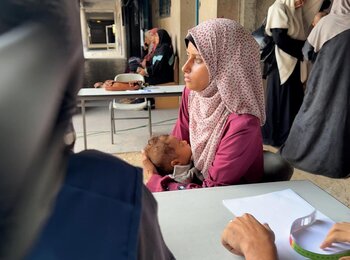 Seven-month-old Iman, with her mother, at a medical point in a school-turned-shelter in Gaza city. She was diagnosed with severe acute malnutrition at six months and UNRWA health teams have been providing her with emergency treatment and supplementary food. Photo by © 2025 UNRWA