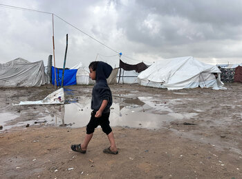 A Palestinian boy walks past tents during a break in the rain in Jabalya, North Gaza. Photo by OCHA