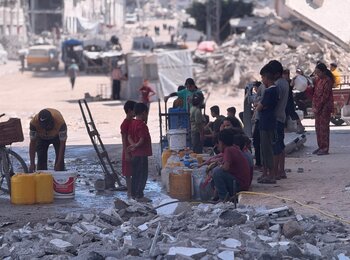 Palestinian children and families gather around a water distribution point amid the rubble in Gaza City. Photo by OCHA/Olga Cherevko