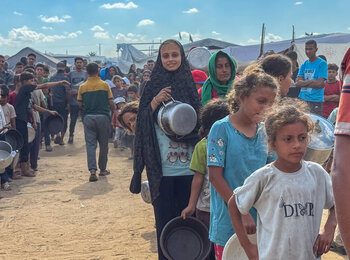 Displaced families queue for a hot meal distribution at a community kitchen in Deir al Balah, Gaza, in October 2025. With renewed hope for a ceasefire, the UN stands ready to scale up life-saving aid delivery across the Gaza Strip. Photo: OCHA/Olga Cherevko