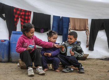 Children sitting outside their tent in Gaza, sharing biscuits delivered by the World Food Programme.  Hundreds of thousands of displaced people are now filling the streets of southern Gaza, living in makeshift shelters in miserable conditions, with little access to food, water, medicines and appropriate shelter. Photo: WFP/Ali Jadallah, January 2024 