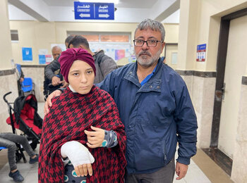אימאן בת ה-16, שנפצעה בתקיפות האחרונות, עומדת ליד אביה שליווה אותה כשפנתה לקבל טיפול רפואי מאונר"א בדיר אל-בלח. צילום: אונר"א.