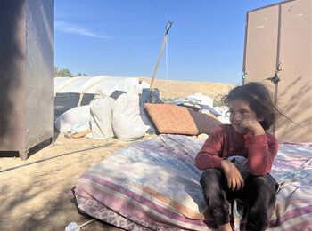 A Palestinian girl sits on a mattress in the open in the Jordan Valley in early February, as her family dismantles their belongings during displacement following repeated settler attacks, which forced nearly 60 community members to flee. Photo by OCHA 