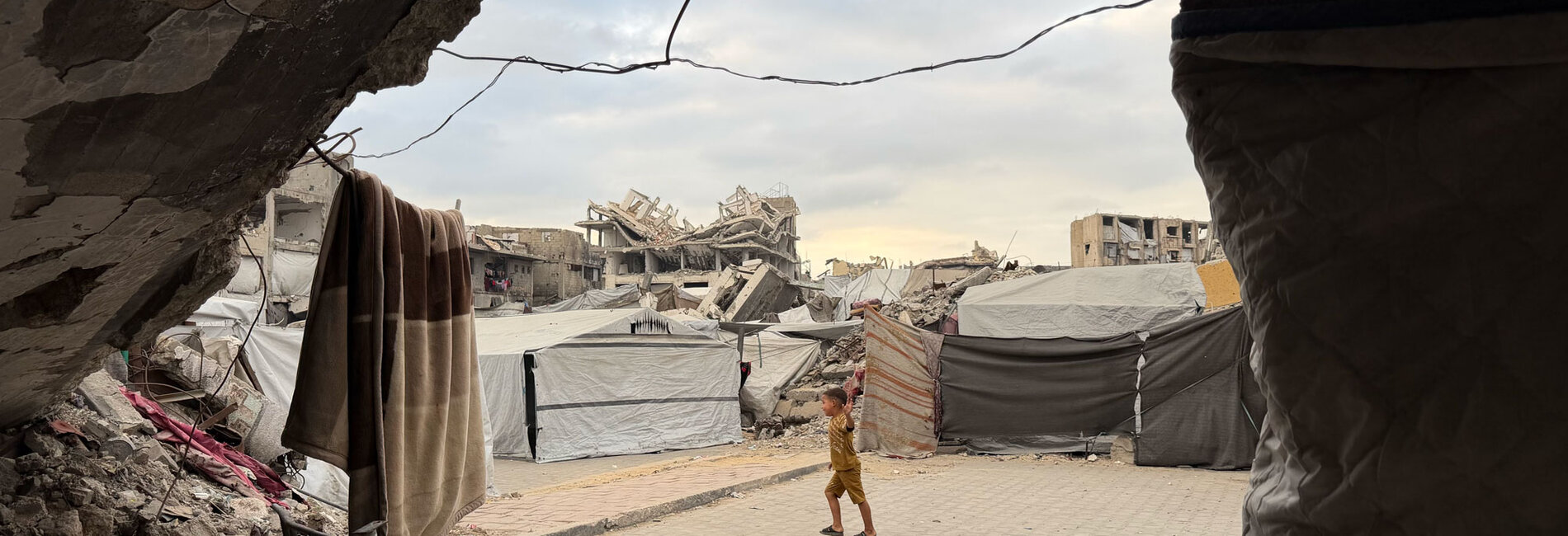 A Palestinian boy playing in between makeshift shelters set up next to unsafe war-damaged buildings at risk of collapse in the Gaza Strip, October 2026. Photo by UN News