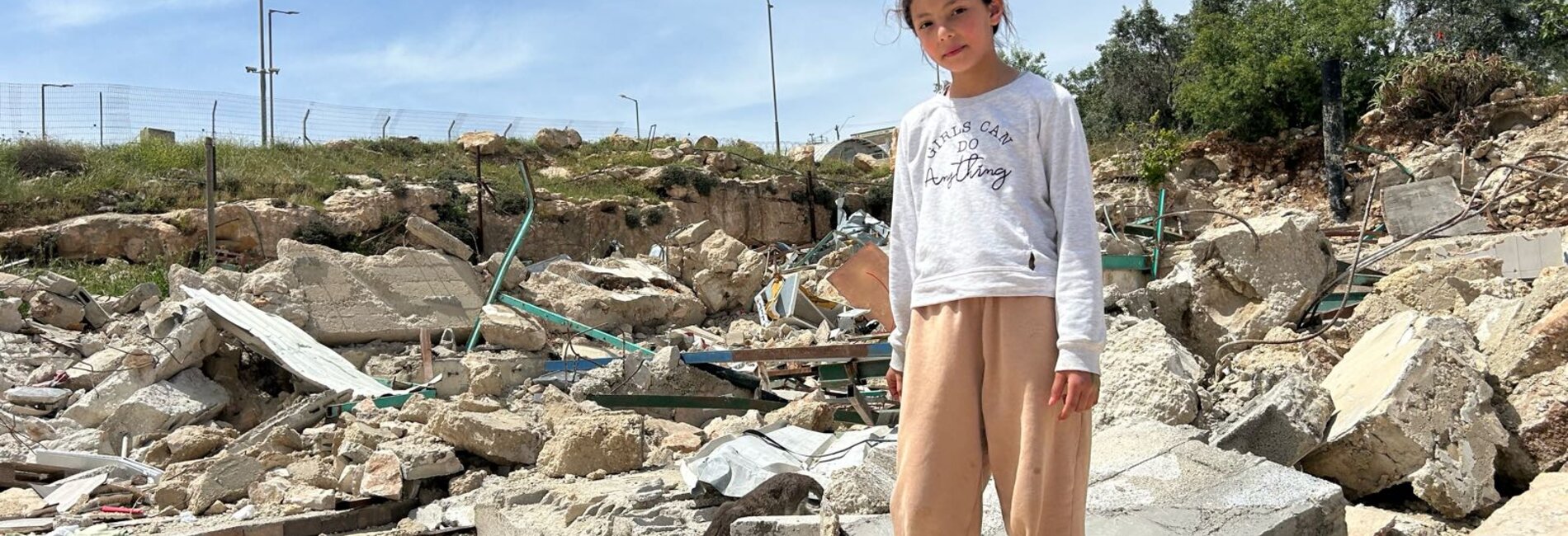 A girl in Az Za’ayyem Bedouin community (Jerusalem governorate) stands on what remains of her home following its demolition by Israeli authorities due to the lack of building permits, which are rarely granted to Palestinians, April 2026. Photo by OCHA