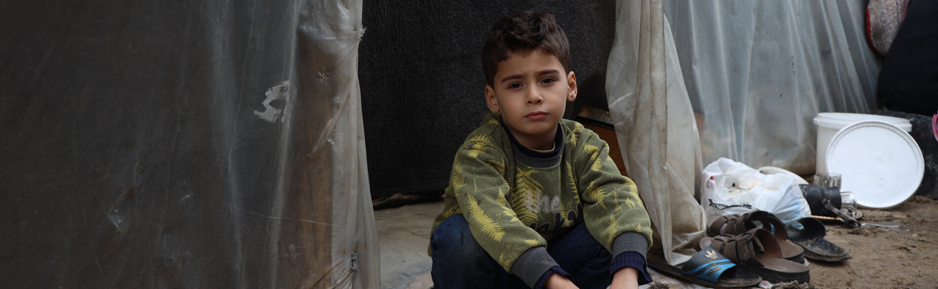 A Palestinian boy sitting next to a makeshift structure in an education facility where displaced families have taken refuge in Gaza. Photo by UNICEF/El Baba