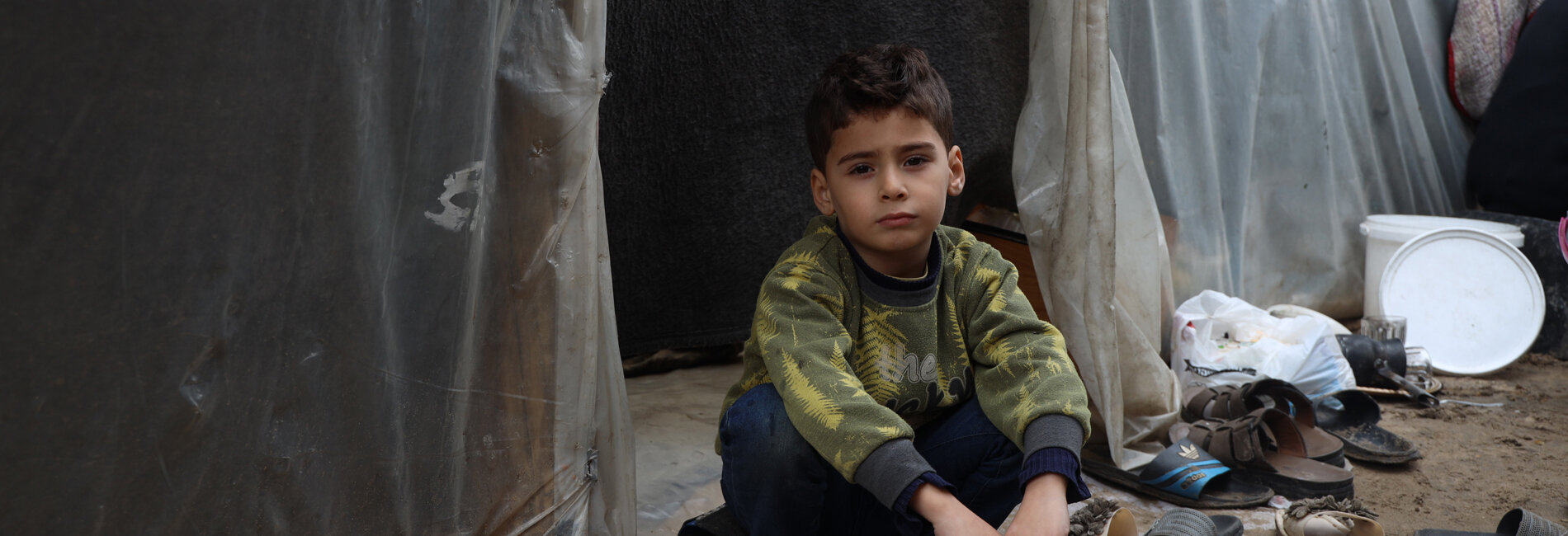 A Palestinian boy sitting next to a makeshift structure in an education facility where displaced families have taken refuge in Gaza. Photo by UNICEF/El Baba