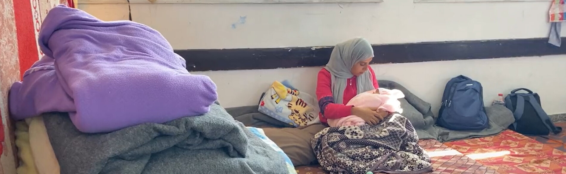 אם פלסטינית והתינוקת שלה, שזה עתה נולדה, בבית ספר המשמש מחסה לעקורים ברצועת עזה. "אין חדר אמבטיה, אין מים ואין טיפול ראוי," היא אומרת. "עוד לא בדקתי או ניקיתי את התפרים של הניתוח הקיסרי." צילום מסך מסרטון וידאו של יוניסף