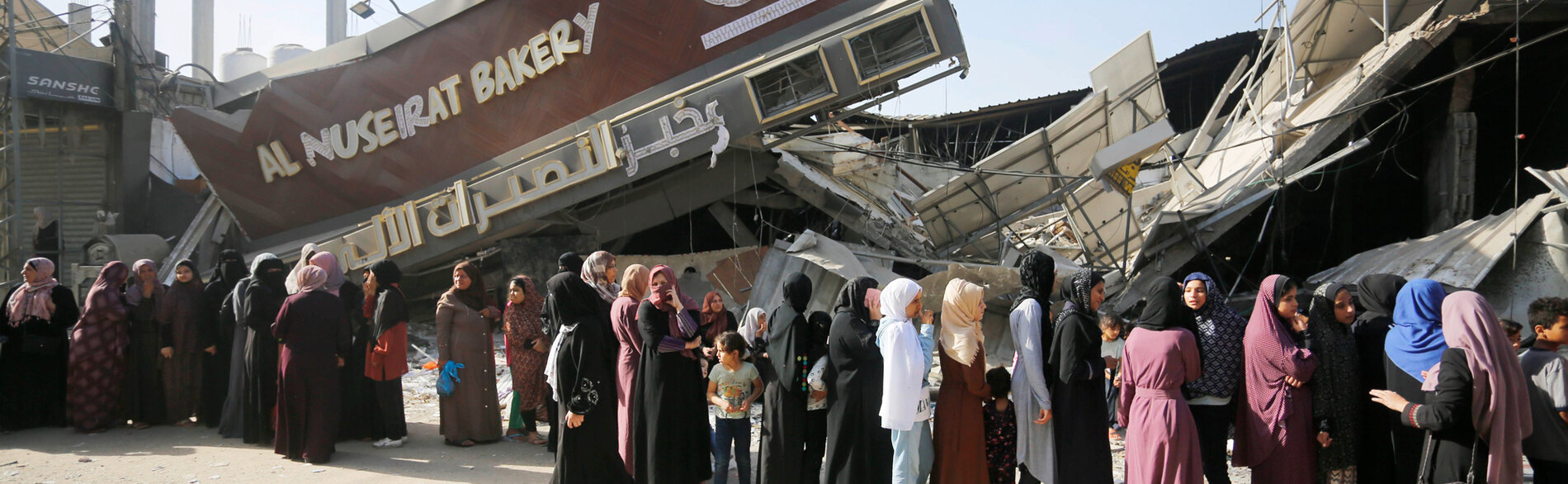 نساء وفتيات يقفن في طوابير أمام مخبز مدمر للحصول على الخبز في قطاع غزة.  قُصف 11 مخبزًا ودُمر منذ 7 تشرين الأول/أكتوبر. وفي جنوب غزة، لا تملك المطحنة الوحيدة العاملة القدرة على طحن القمح بسبب انقطاع الكهرباء والوقود. تصوير الأونروا