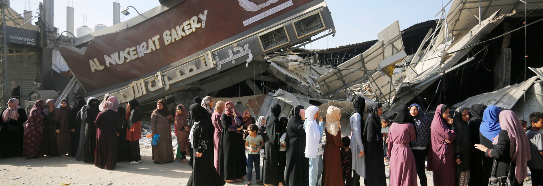 نساء وفتيات يقفن في طوابير أمام مخبز مدمر للحصول على الخبز في قطاع غزة.  قُصف 11 مخبزًا ودُمر منذ 7 تشرين الأول/أكتوبر. وفي جنوب غزة، لا تملك المطحنة الوحيدة العاملة القدرة على طحن القمح بسبب انقطاع الكهرباء والوقود. تصوير الأونروا