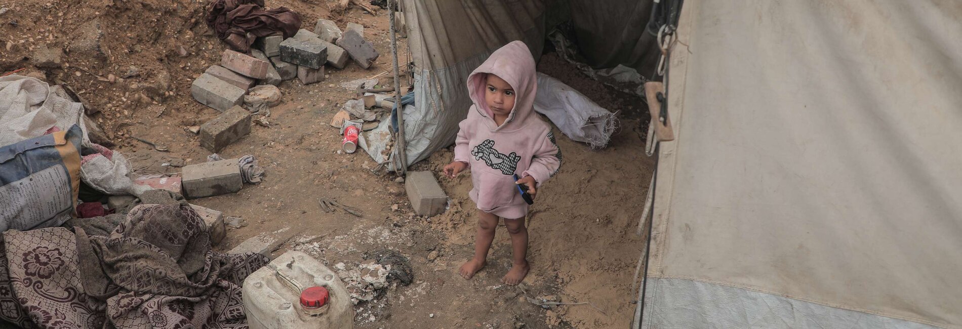 A toddler stands amid debris and personal belongings outside a tent in the Gaza Strip. Photo by UNICEF.