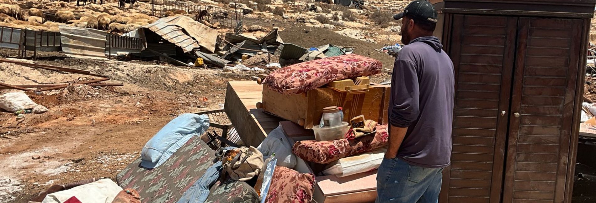A Palestinian man next to some of his belongings, out in the open, following the demolition of 20 homes and other structures in Al Mughayyir. Photo by OCHA