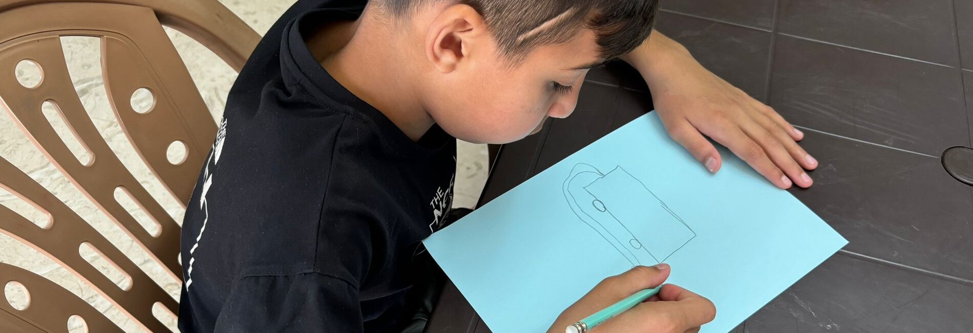 Kareem drawing a fire truck, sharing his dream of becoming a fireman. Three months ago, limited by his injury, he wished to be a carpenter. With nearly 90% recovery, his hopes have shifted back to firefighting, reflecting his progress and renewed sense of hope. Photo by © EJYMCA/Maha Sabbah