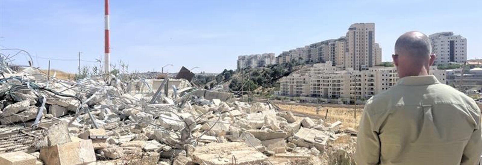 A displaced Palestinian man from Umm Tuba village, East Jerusalem, overlooks the nearby Israeli settlement of Har Homa after Israeli forces demolished his house. Photo by OCHA