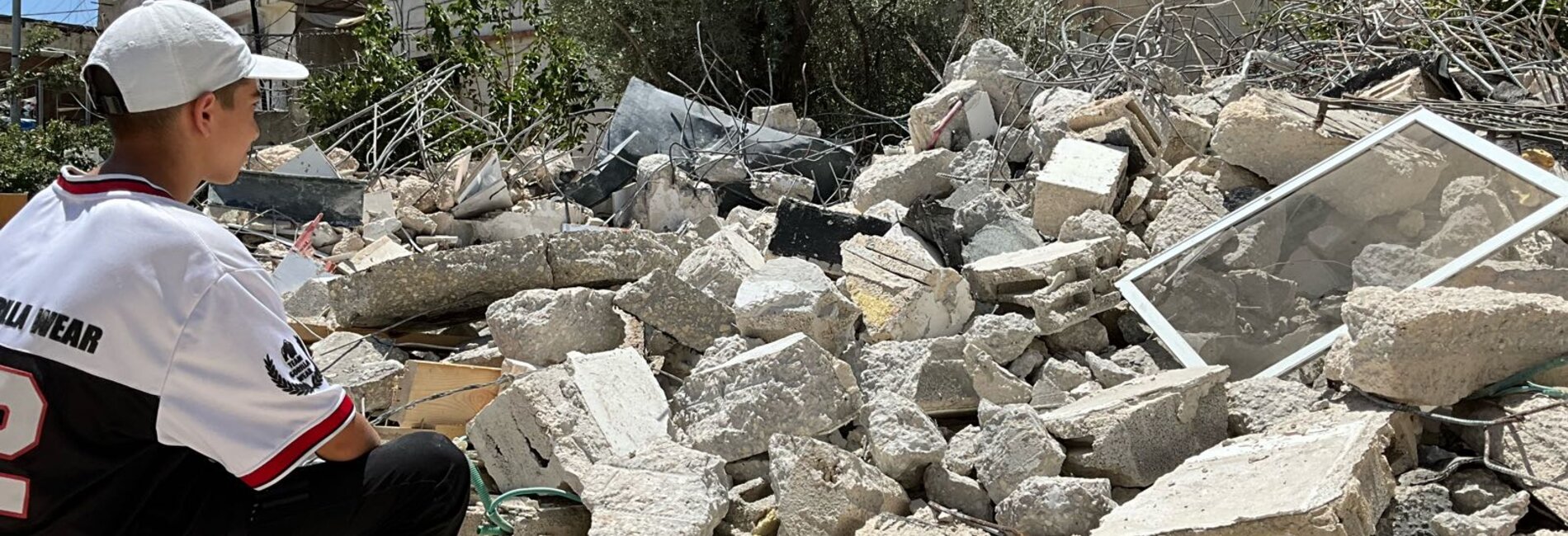 Palestinian boy sitting in front of a home demolished by its owners following Israeli orders in Silwan area of East Jerusalem. Photo by OCHA