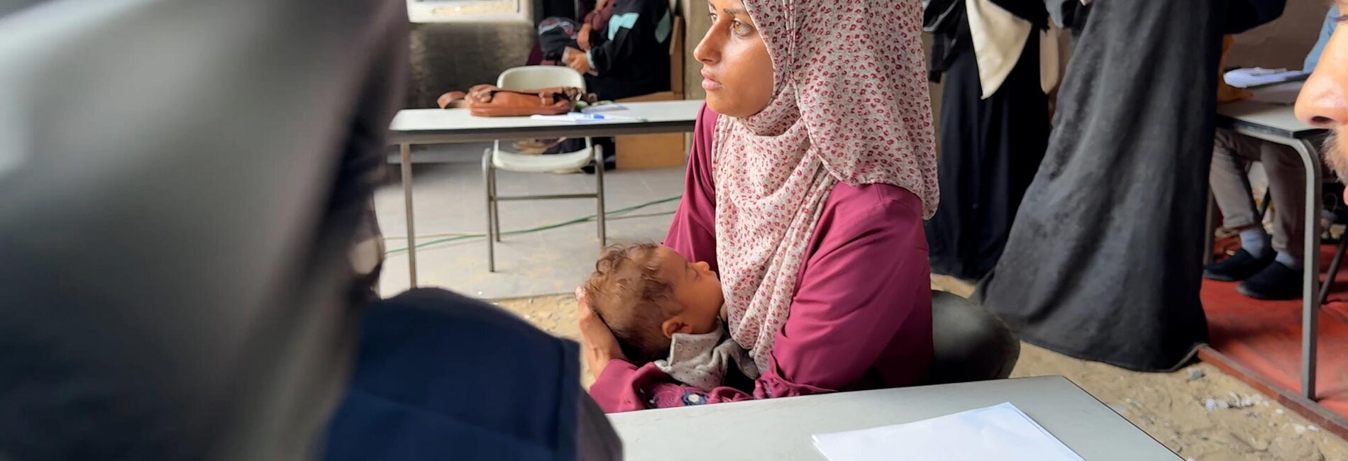 Seven-month-old Iman, with her mother, at a medical point in a school-turned-shelter in Gaza city. She was diagnosed with severe acute malnutrition at six months and UNRWA health teams have been providing her with emergency treatment and supplementary food. Photo by © 2025 UNRWA