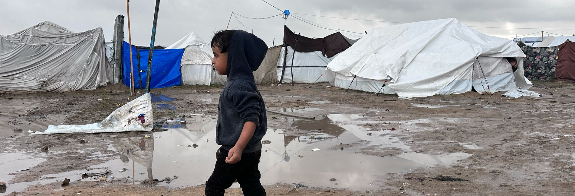 A Palestinian boy walks past tents during a break in the rain in Jabalya, North Gaza. Photo by OCHA