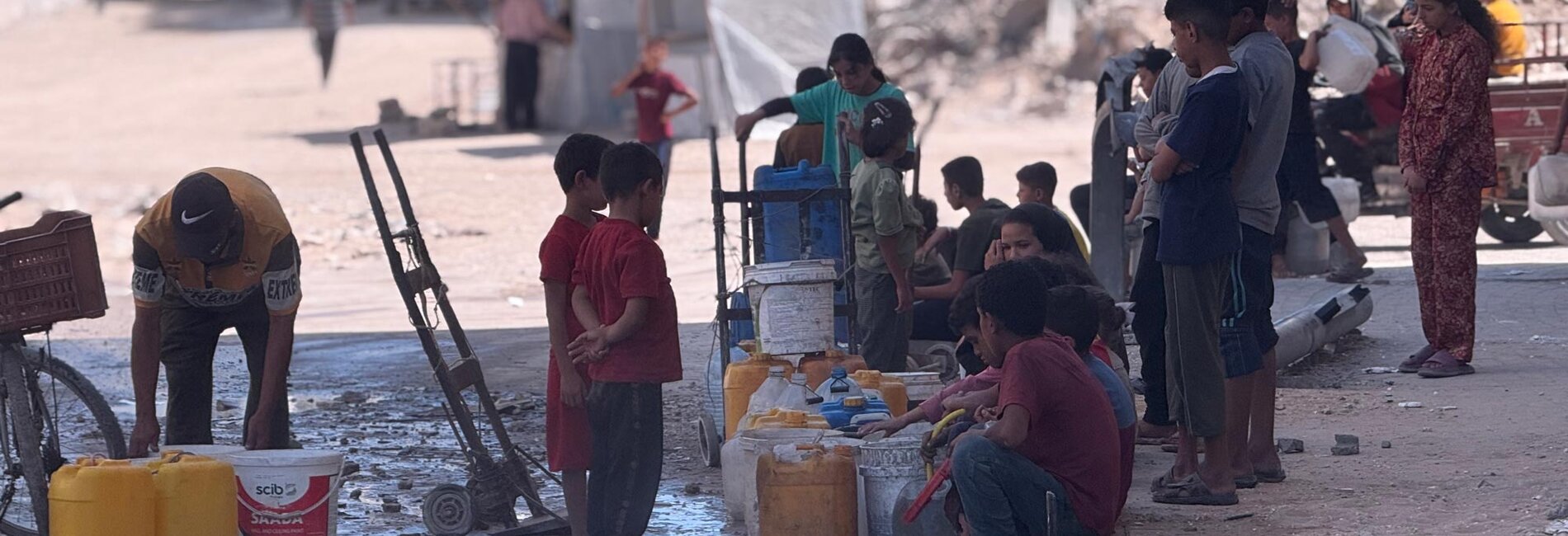 Palestinian children and families gather around a water distribution point amid the rubble in Gaza City. Photo by OCHA/Olga Cherevko