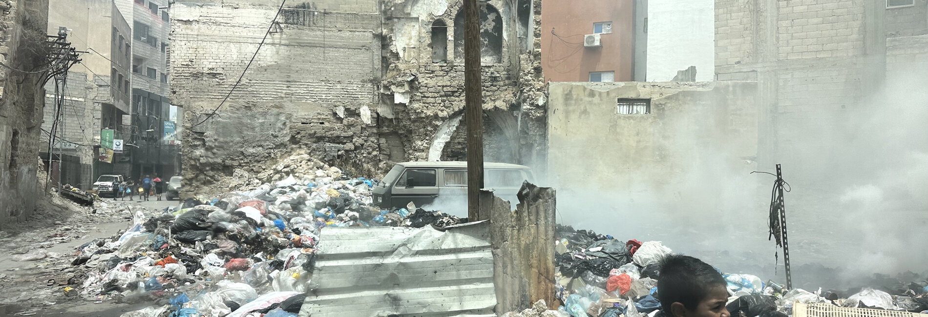 A boy walking next to scattered solid waste in a heavily damaged area of Gaza city. Photo by OCHA/Olga Cherevko, 25 April 2024