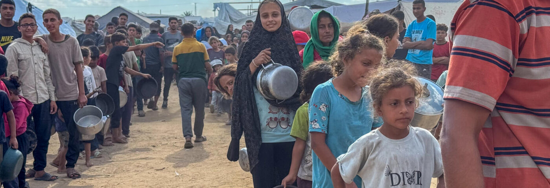 Displaced families queue for a hot meal distribution at a community kitchen in Deir al Balah, Gaza, in October 2025. With renewed hope for a ceasefire, the UN stands ready to scale up life-saving aid delivery across the Gaza Strip. Photo: OCHA/Olga Cherevko
