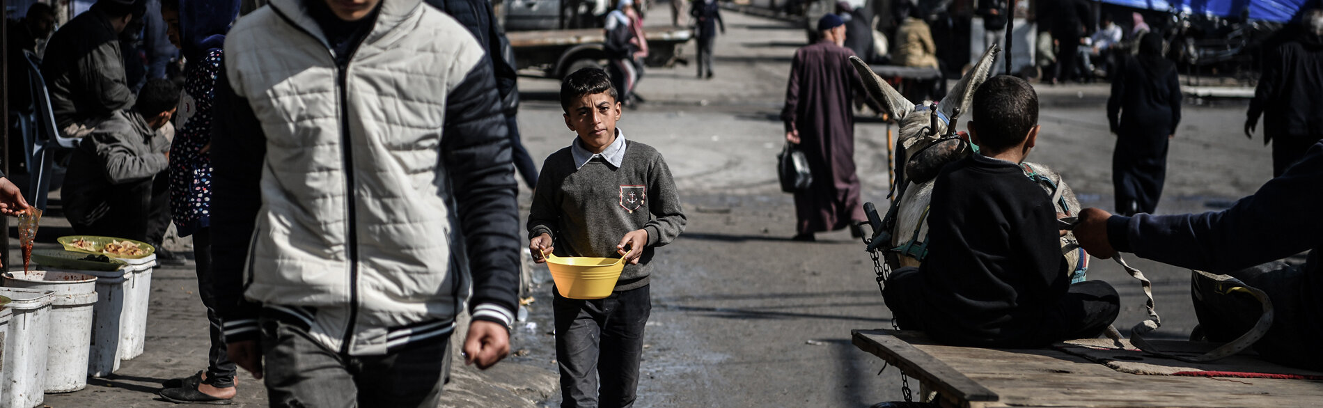 محمد (11 عامًا) يحمل وعاء من الفاصوليا لأسرته التي تقيم في خيمة في رفح. يقول: «كل يوم، أمشي كيلومترين وأقضي أكثر من خمس ساعات فقط لتوفير وجبة واحدة في اليوم لأسرتي.» تصوير اليونيسف/زقوت