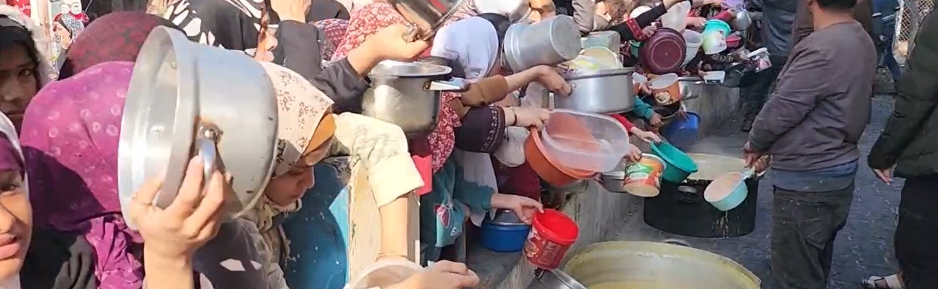 Women and girls in Rafah, southern Gaza Strip, holding pots and other empty containers in front of a group of volunteers preparing soup for displaced families. On 22 December, the Secretary-General warned that ”widespread famine looms,” following the Integrated Phase Classification (IPC) Special Briefs produced by the IPC global initiative on Gaza. Screenshot from a video by UNICEF