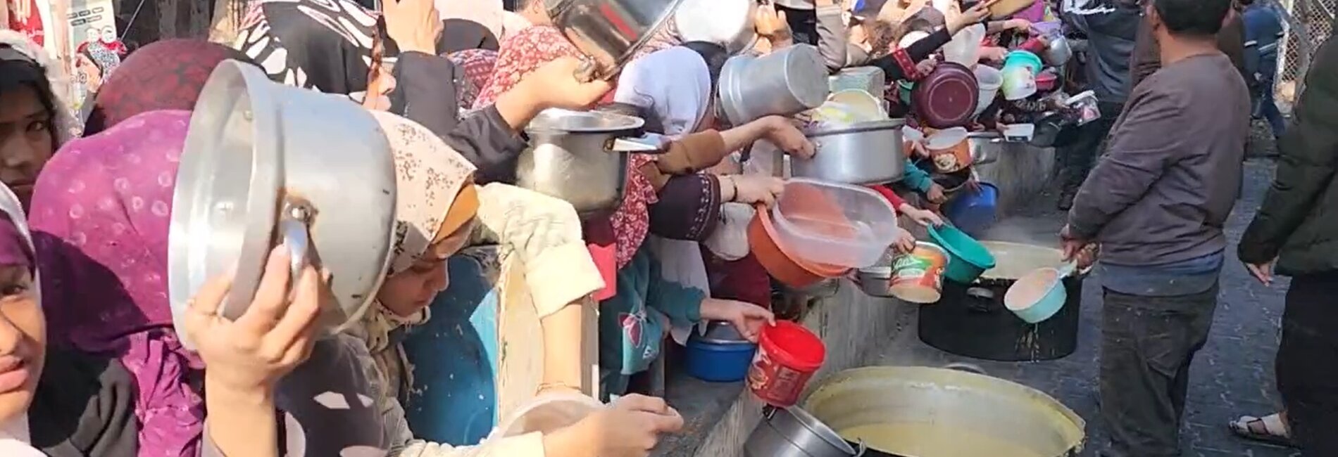 Women and girls in Rafah, southern Gaza Strip, holding pots and other empty containers in front of a group of volunteers preparing soup for displaced families. On 22 December, the Secretary-General warned that ”widespread famine looms,” following the Integrated Phase Classification (IPC) Special Briefs produced by the IPC global initiative on Gaza. Screenshot from a video by UNICEF