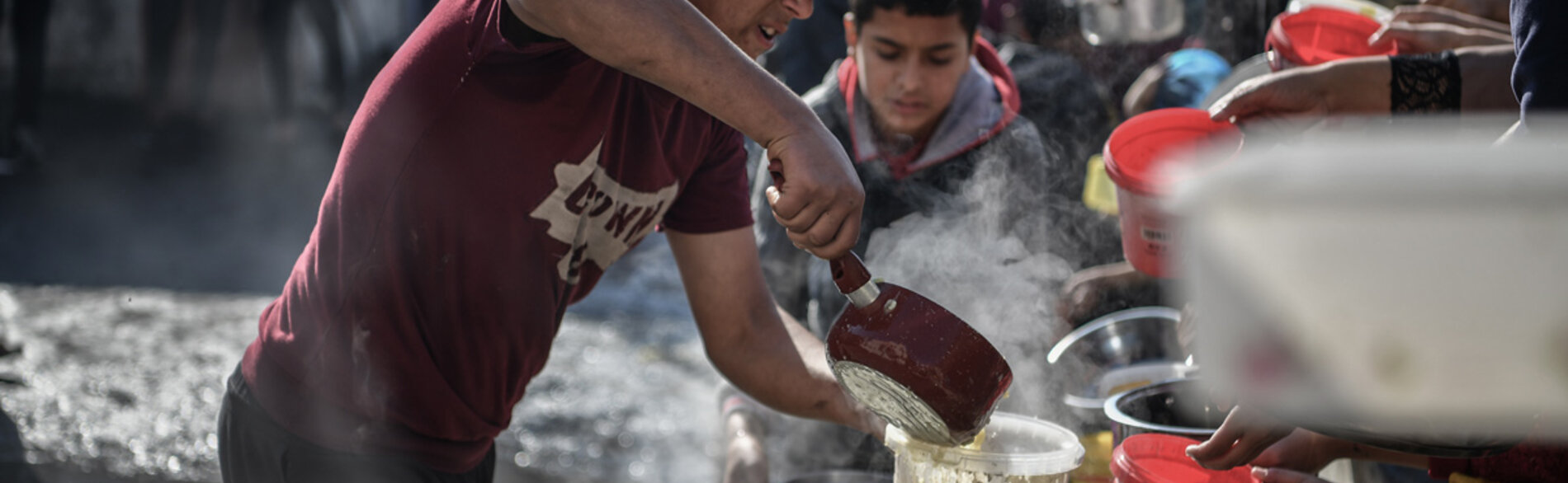 متطوع يوزع الطعام على الناس في رفح، جنوب غزة. ويواجه ما لا يقل عن 576,000 إنسان في غزة – ربع سكانها – مستويات كارثية من انعدام الأمن الغذائي ويتعرّضون لخطر المجاعة. تصوير اليونيسف/عبد زقوت