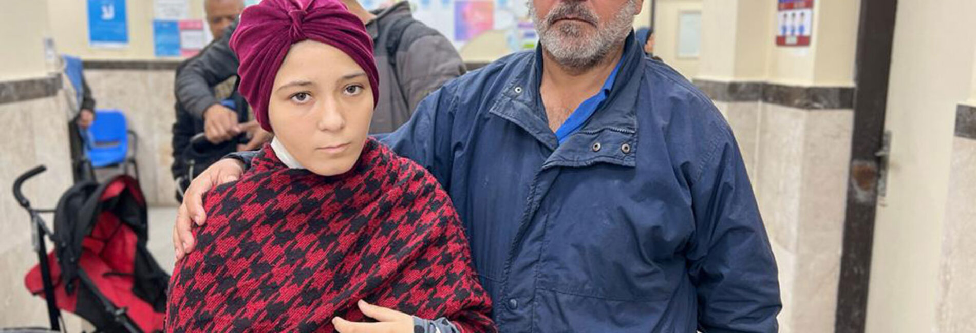 Sixteen-year-old Eman, injured in recent strikes, stands beside her father who accompanied her to receive medical care from UNRWA in Deir Al Balah. Photo by of UNRWA