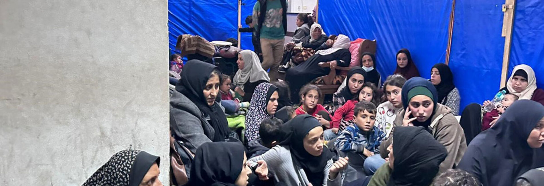 Women and children squeezing into a limited space at an overcrowded UNRWA facility in Khan Younis, amid nearby gunfire and shelling. Photo by UNRWA/Hussein Owda, 23 January 2024 