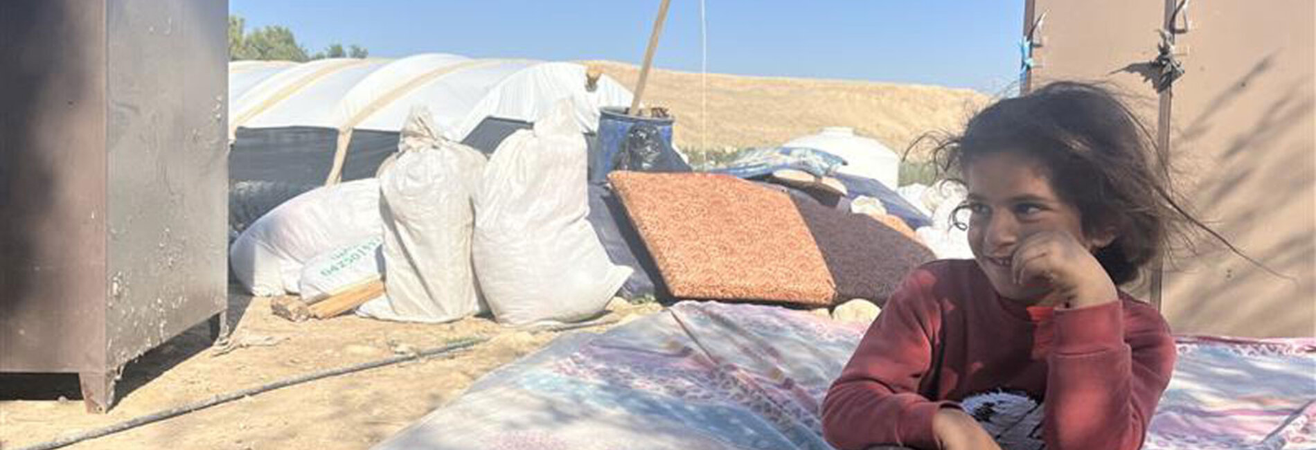 A Palestinian girl sits on a mattress in the open in the Jordan Valley in early February, as her family dismantles their belongings during displacement following repeated settler attacks, which forced nearly 60 community members to flee. Photo by OCHA 