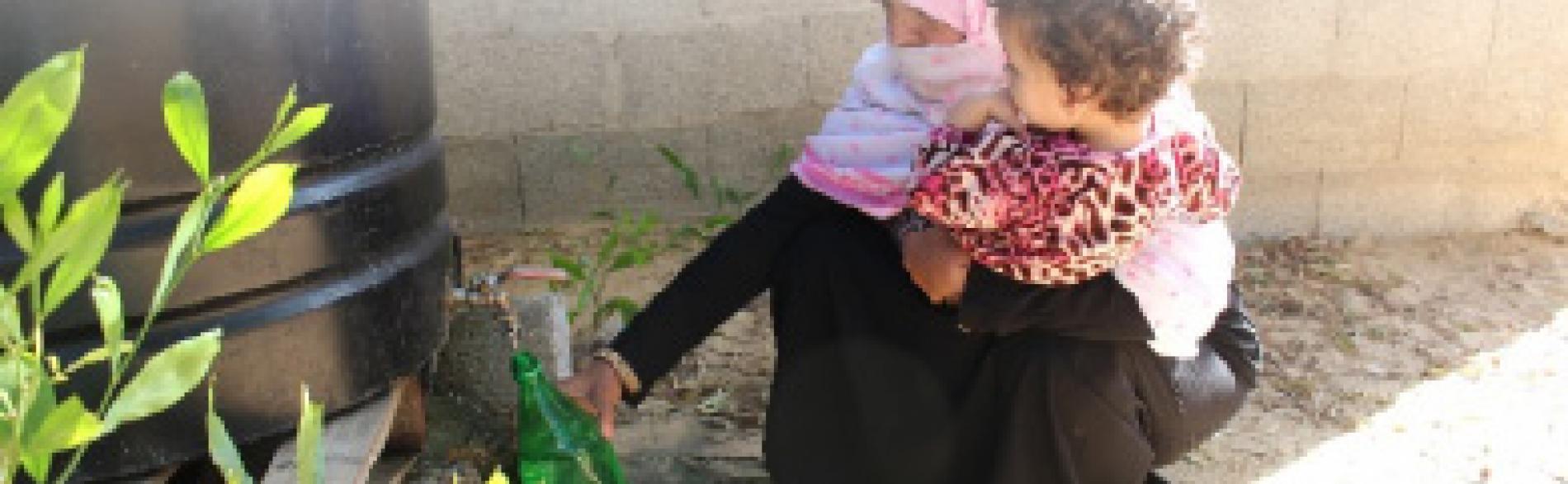 منى وهي تملأ زجاجة من المياه غير الصالحة للشرب من خزان في ساحة منزلها. © - تصوير منظمة أوكسفام