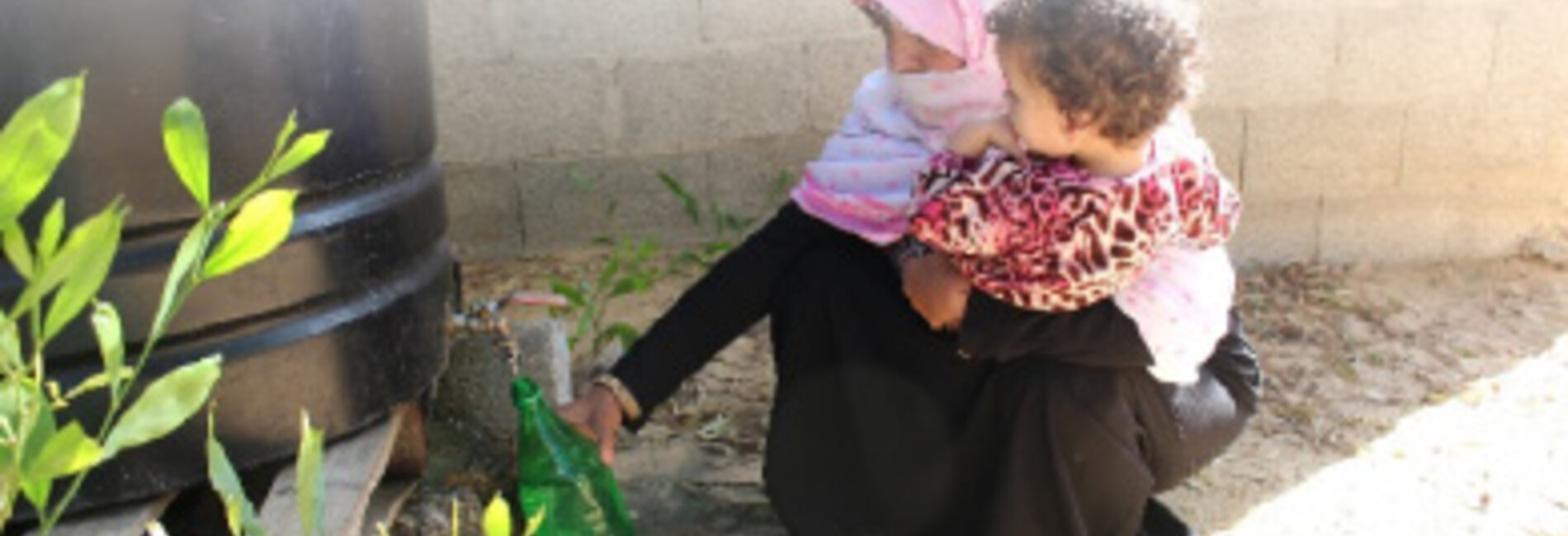 Mona filling a bottle of non-potable water from a tank in her yard. © Photo by OXFAM