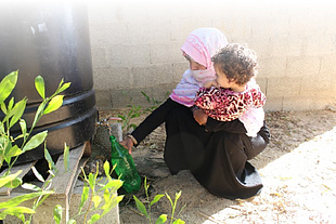 Mona filling a bottle of non-potable water from a tank in her yard. © Photo by OXFAM