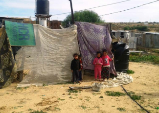 Children standing in front of a temporary shelter made of cloths in Gaza, January 2016