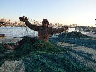 Palestinian boy handling a fishing net in Gaza harbour, December 2015. Photo by OCHA