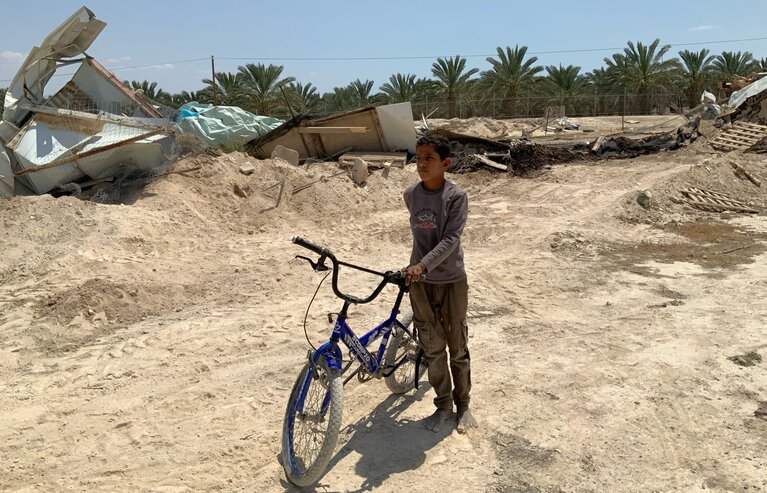 A boy in Deir Hajla (Jericho governorate) stands with his bicycle next to the remains of structures demolished by Israeli authorities due to the lack of building permits, which are rarely granted to Palestinians, April 2026. Photo by OCHA