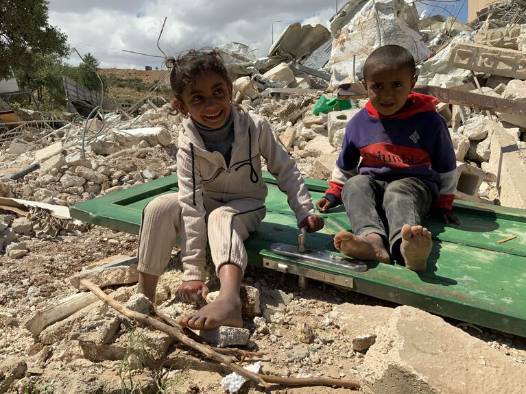 Children from the Jaba’ Bedouin community sit on what remains of a home that Israeli forces demolished for lacking Israeli permits that are nearly impossible for Palestinians to obtain, May 2026. Photo by OCHA 