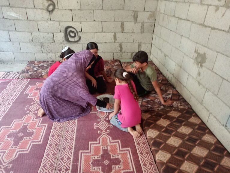 Ghada and her children sitting on the newly bought plastic mat and mattresses, September 2020. Photo by SIF