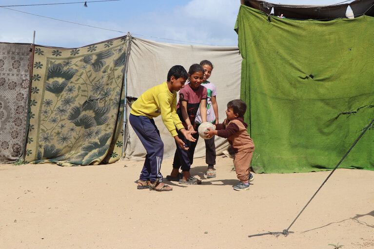Rasheed* playing with his siblings outside their tent in Deir al Balah, Gaza. 