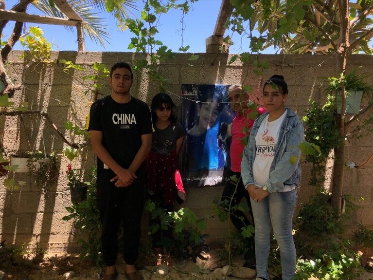 Kamal and three of his children. On the wall is a photo of his son Ibrahim who was killed in the escalation of 2008/09. Beit Lahiya, 7 July 2021. Photo by OCHA.