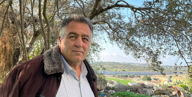 Tayseer Amarneh standing near an olive tree in the ”West Bank” side of the Barrier. Photo by OCHA, December 2023