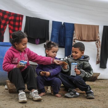 Children sitting outside their tent in Gaza, sharing biscuits delivered by the World Food Programme.  Hundreds of thousands of displaced people are now filling the streets of southern Gaza, living in makeshift shelters in miserable conditions, with little access to food, water, medicines and appropriate shelter. Photo: WFP/Ali Jadallah, January 2024 